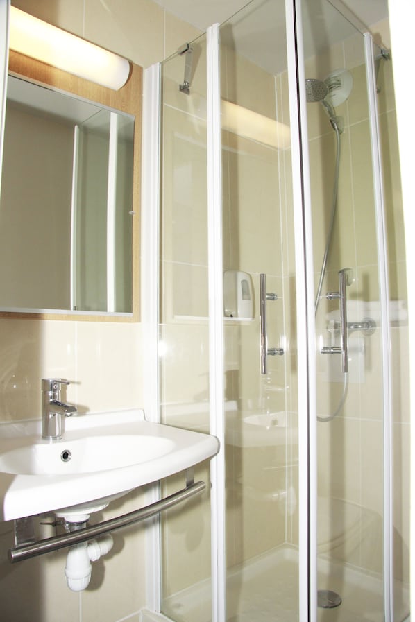 A bathroom with a glass-enclosed shower, a sink, and a mirror. - Hôtel Inn Design Vierzon (Vierzon)
