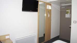 A hotel room with a television, a mirror, a door, and a radiator.