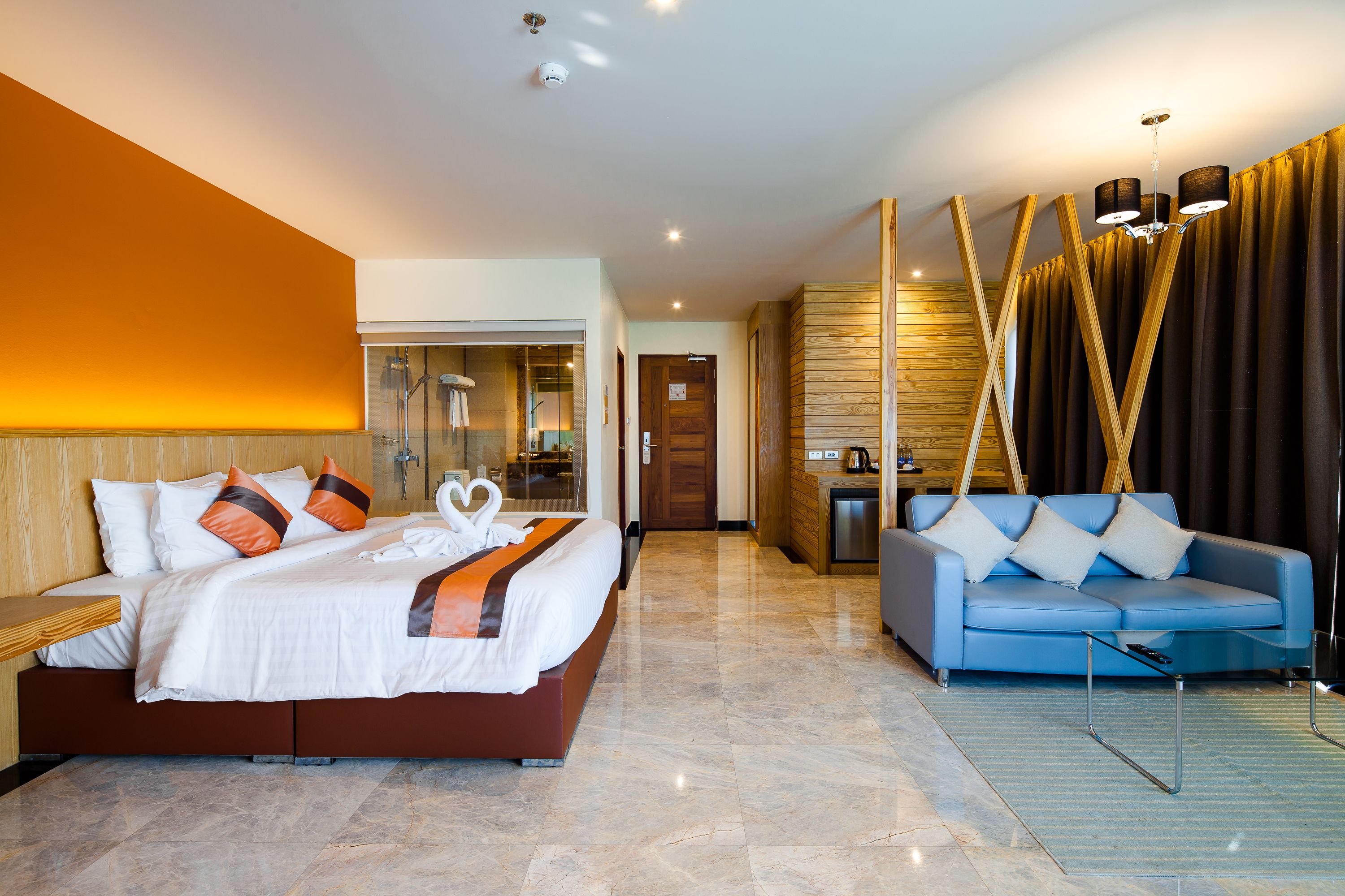 A modern hotel room with a large bed, a blue sofa, and a wooden accent wall.