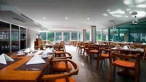 A spacious dining area with multiple tables and chairs, large windows offering a view of greenery, and a modern interior design. - Balihai Bay (Pattaya)