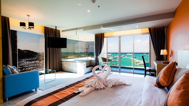 A hotel room with a large bed, a blue sofa, a TV, and a view of the sea. - Balihai Bay (Pattaya)