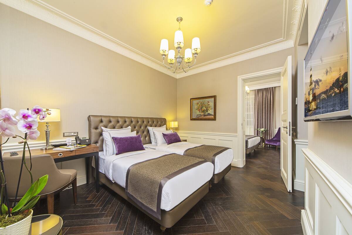 A hotel room with a large bed, a desk with a lamp, a chair, and a potted plant.