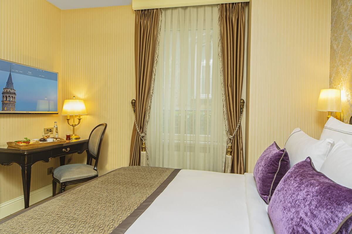 A hotel room with a bed, a desk, a chair, and a television displaying a cityscape.
