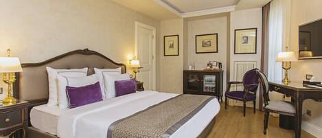 A hotel room with a large bed, two bedside tables with lamps, a desk with a chair, and framed pictures on the walls.