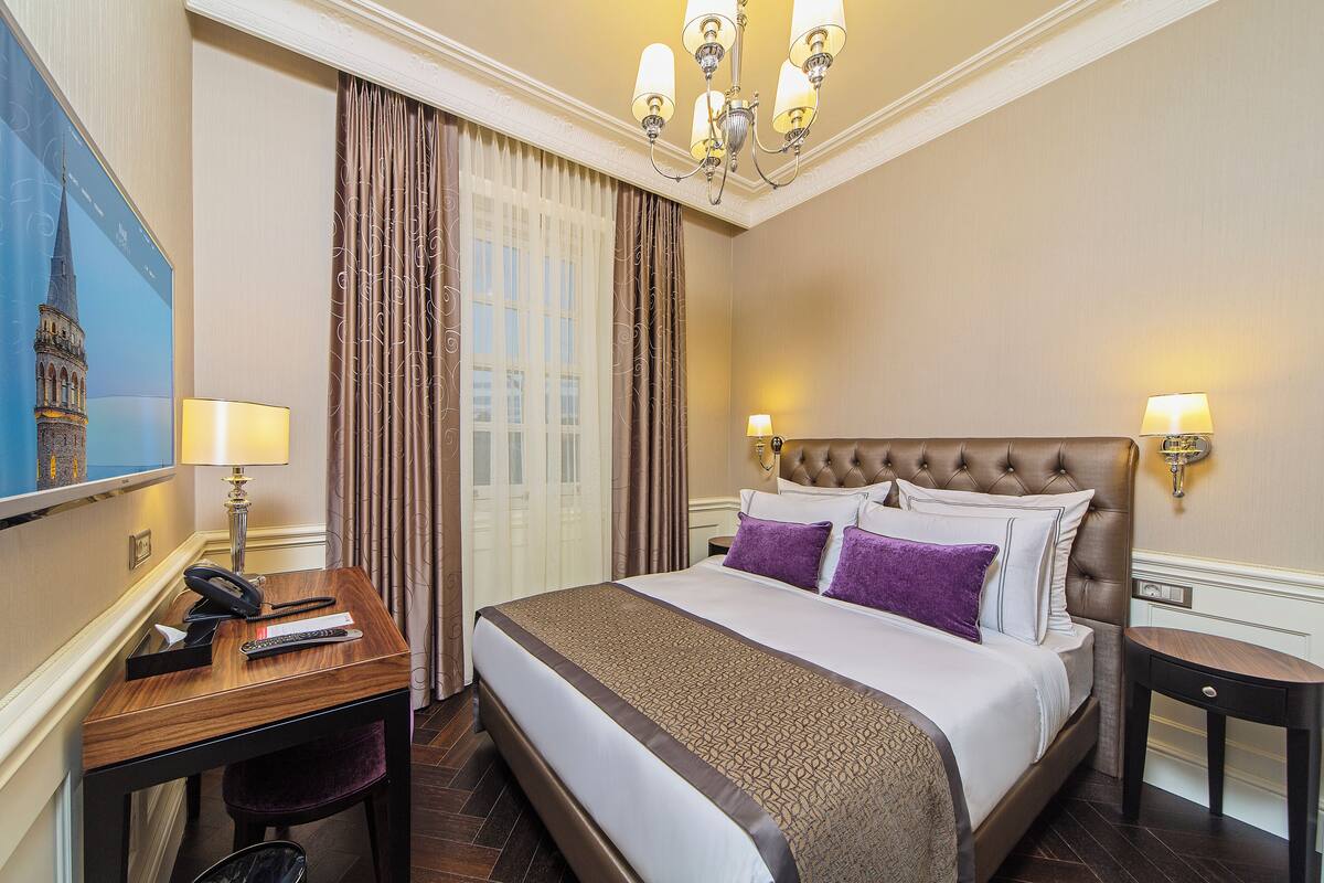 A hotel room with a large bed, a desk with a telephone, and a chair.