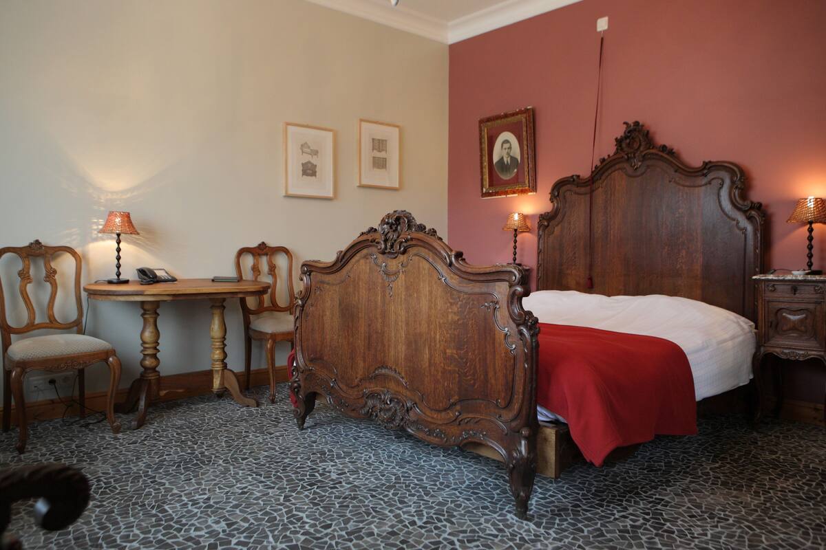 A bedroom with a large wooden bed, a small round table, two chairs, and a lamp.