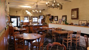 Een eetgedeelte met houten tafels en stoelen, een bar met een toog, en een kruis aan de muur.