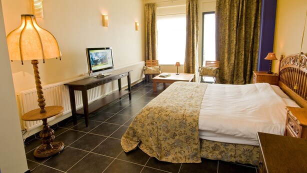 Een hotelkamer met een bed, bureau, stoel, televisie en gordijnen.