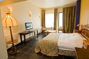 Habitación de hotel con cama, escritorio, silla, televisor y cortinas.