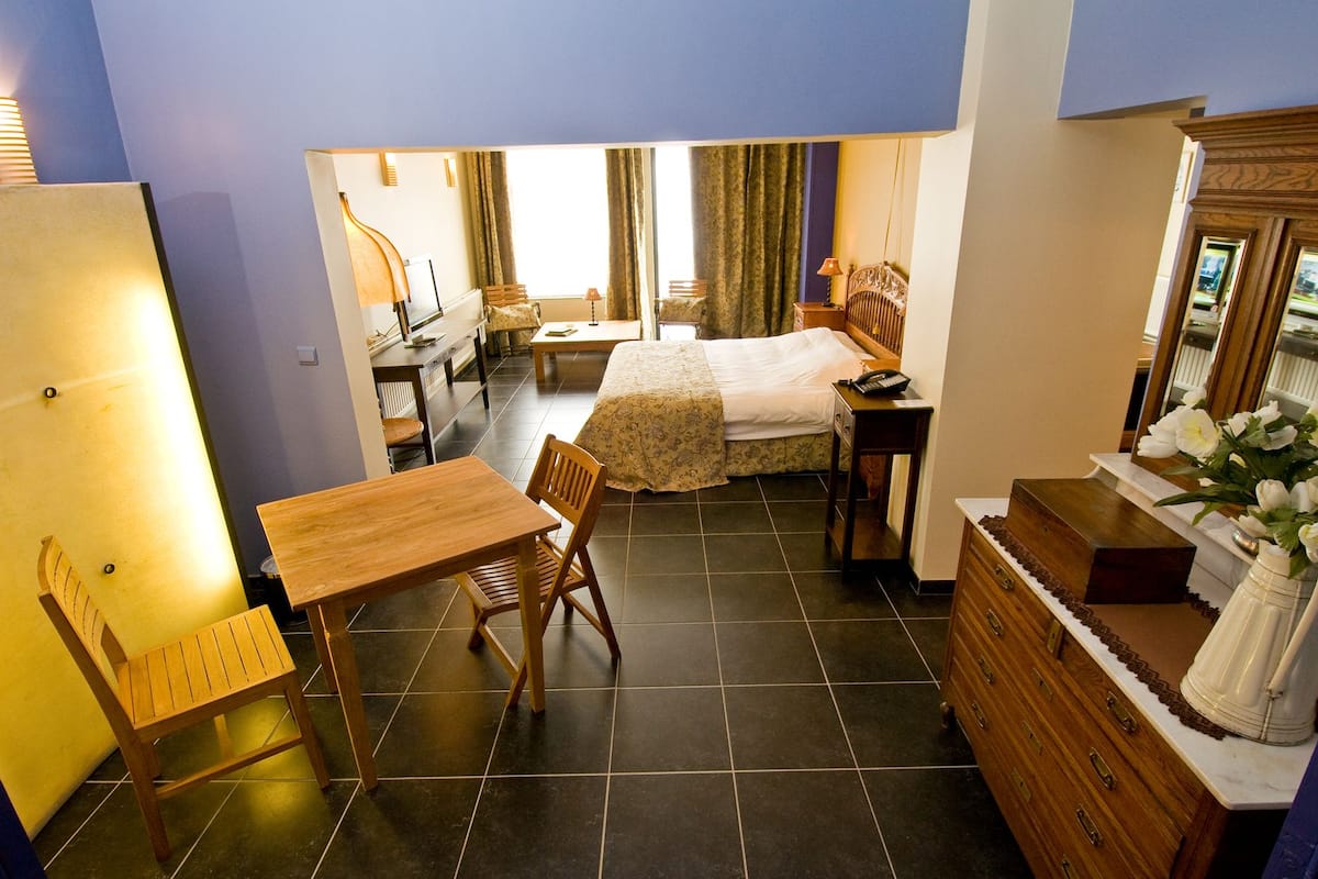 A compact hotel room with a bed, a desk, a chair, a dresser, and a mirror.