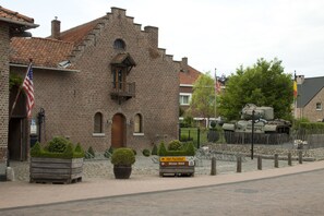 Un edificio histórico de ladrillo con una torre, un cartel que indica 'Het Pachthof Winter 1944' y un tanque militar exhibido.