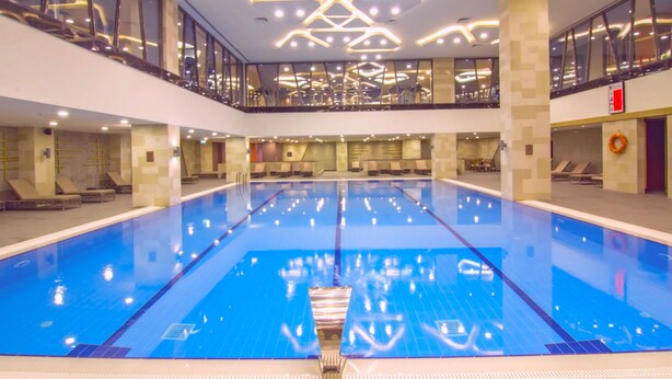Una amplia piscina interior de diseño moderno, rodeada por una barandilla de vidrio y un balcón en un segundo piso.