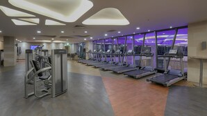 Un gimnasio moderno con cintas de correr, máquinas de pesas y un amplio ventanal con vistas al paisaje urbano.