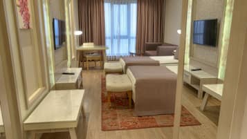 A hotel room with a bed, a desk, a chair, a sofa, a TV, and a window with curtains.