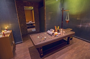 Un lettino da massaggio con candele, un asciugamano e diversi strumenti per massaggi in una stanza di spa con uno specchio e una parete strutturata.