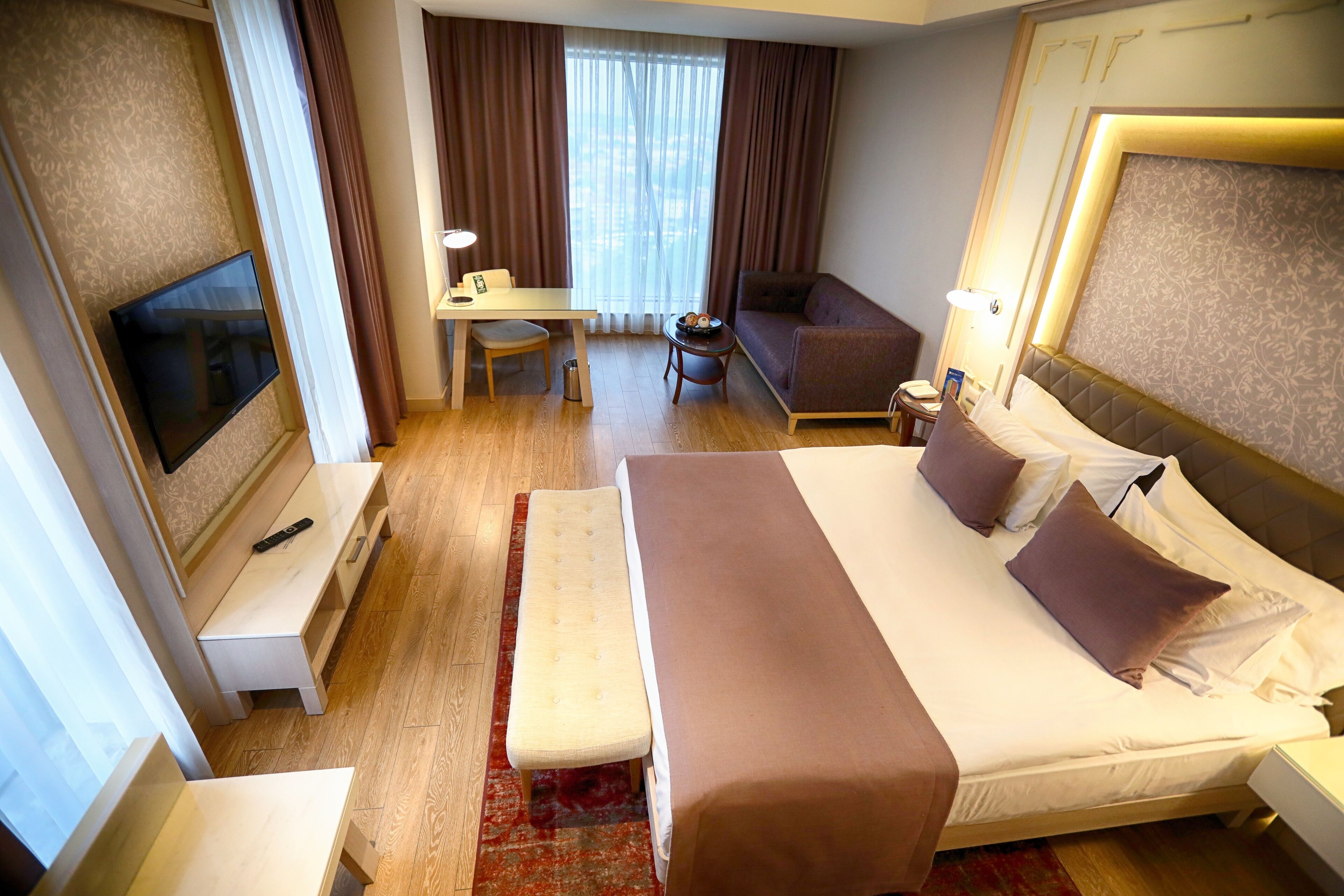 A hotel room with a large bed, a desk, a chair, a TV, and a sofa.