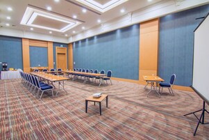 Una sala de conferencias con una larga mesa, sillas, un proyector y piso alfombrado.