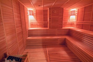 A sauna with wooden benches and benches, a sloped floor, and a door with a circular emblem.