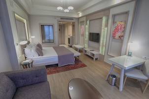 A modern hotel room with a bed, a sofa, a desk, and a TV.