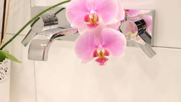 A bathroom with a modern chrome faucet and a potted orchid plant.