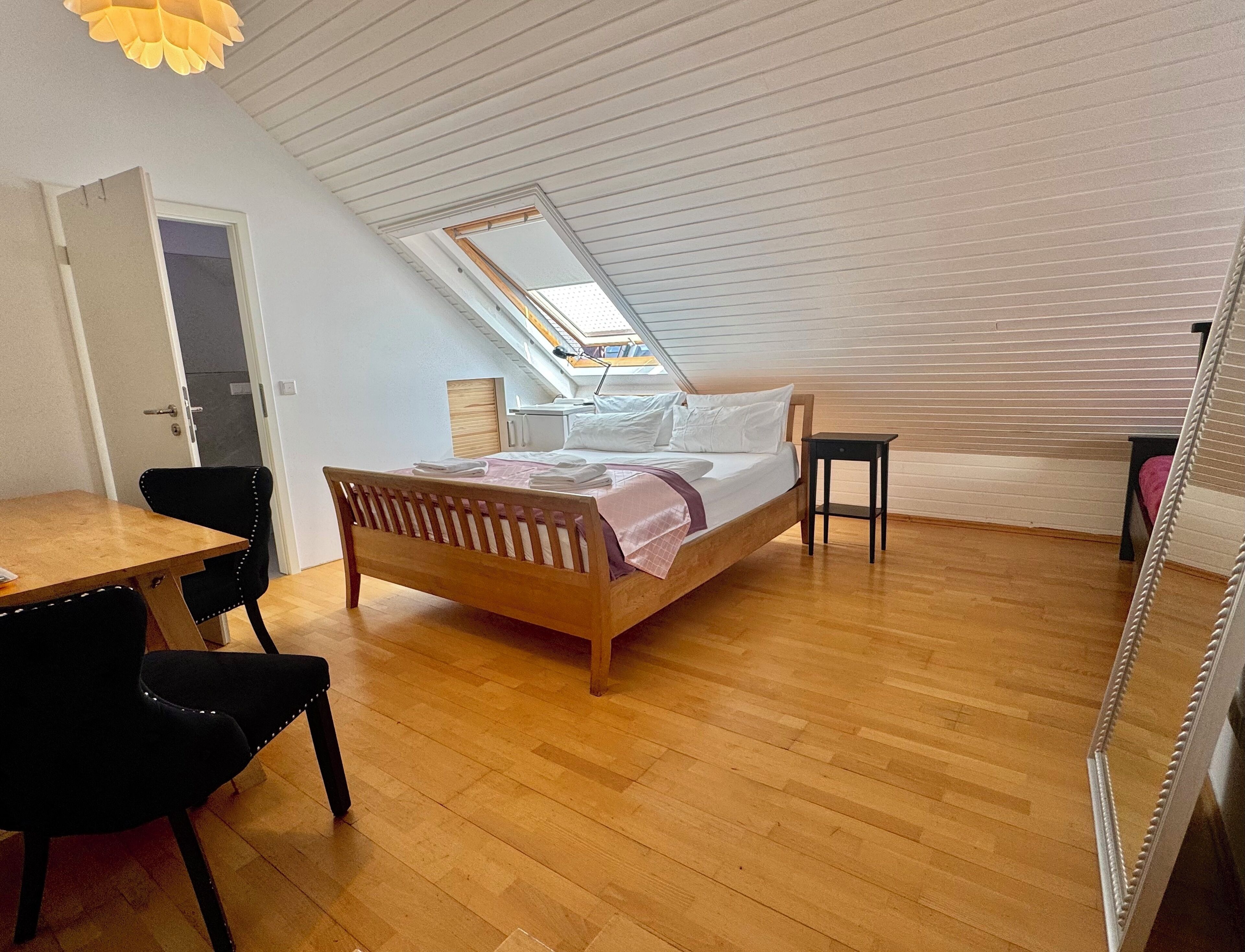 A bedroom with a wooden bed, a desk, and a chair. There is a skylight above the bed.
