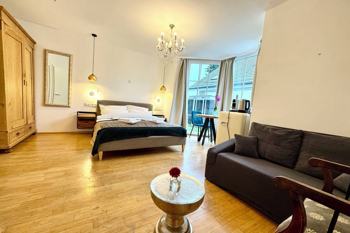 Een moderne slaapkamer met een bed, een bank, een kleine tafel met een bloem, een kledingkast en een raam met gordijnen.