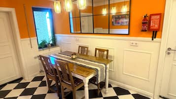 A dining area with a checkered floor, wooden chairs, a table with a striped tablecloth, pendant lights, a mirror, and a fire extinguisher.
