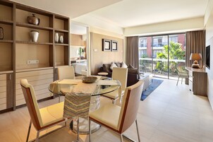 Una sala de estar moderna con una mesa de comedor de vidrio, asientos cómodos, un sofá y un balcón con vistas a edificios y vegetación.