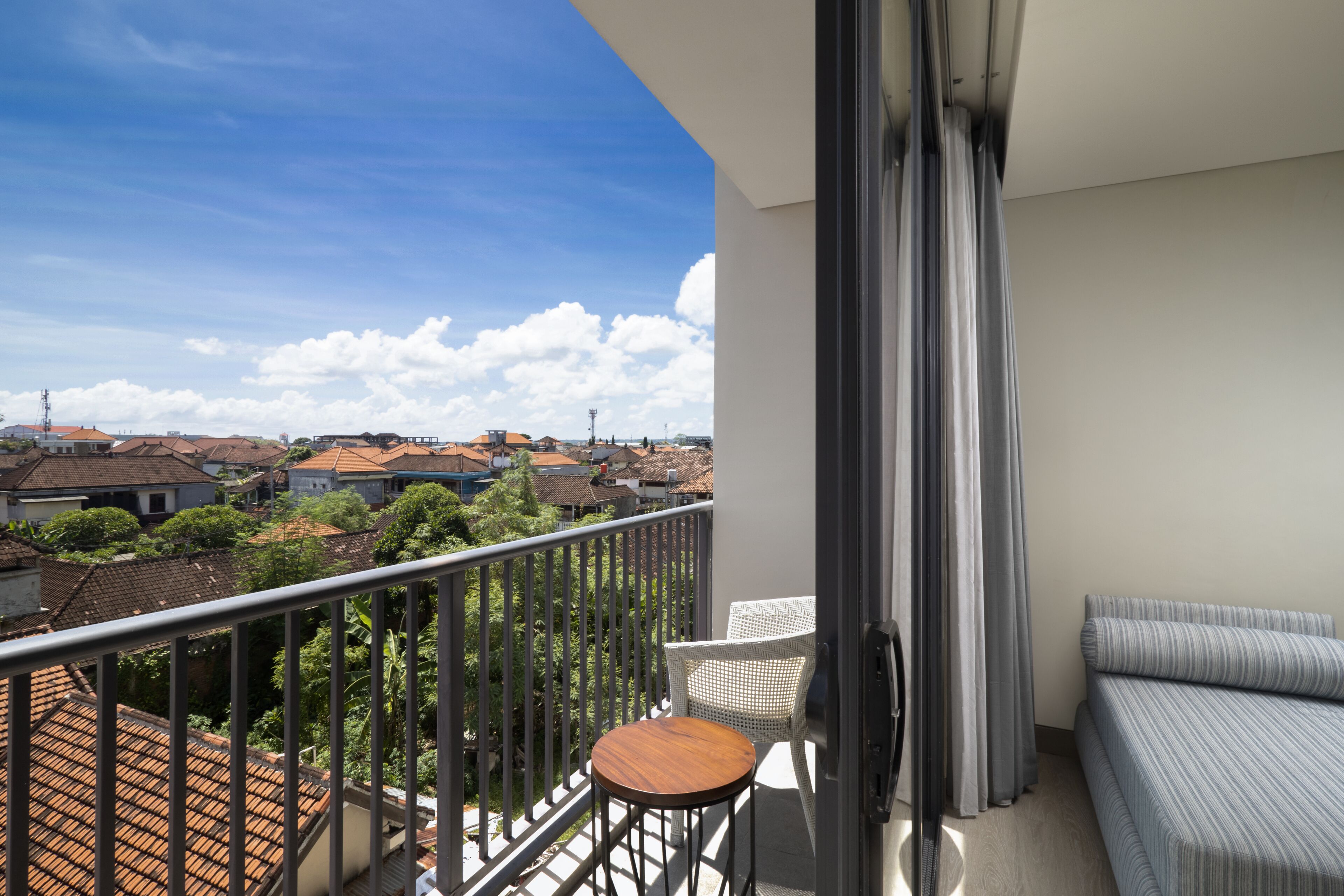 A balcony with a view of a residential area, a small round table, and a sofa.