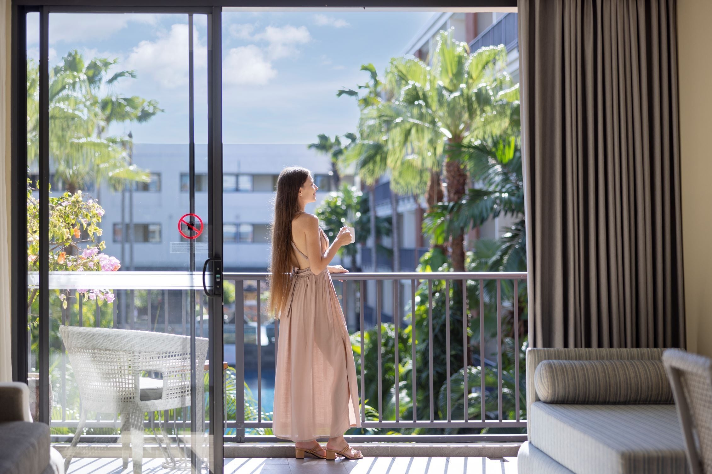 Una mujer parada en un balcón con vista a palmeras y un edificio.