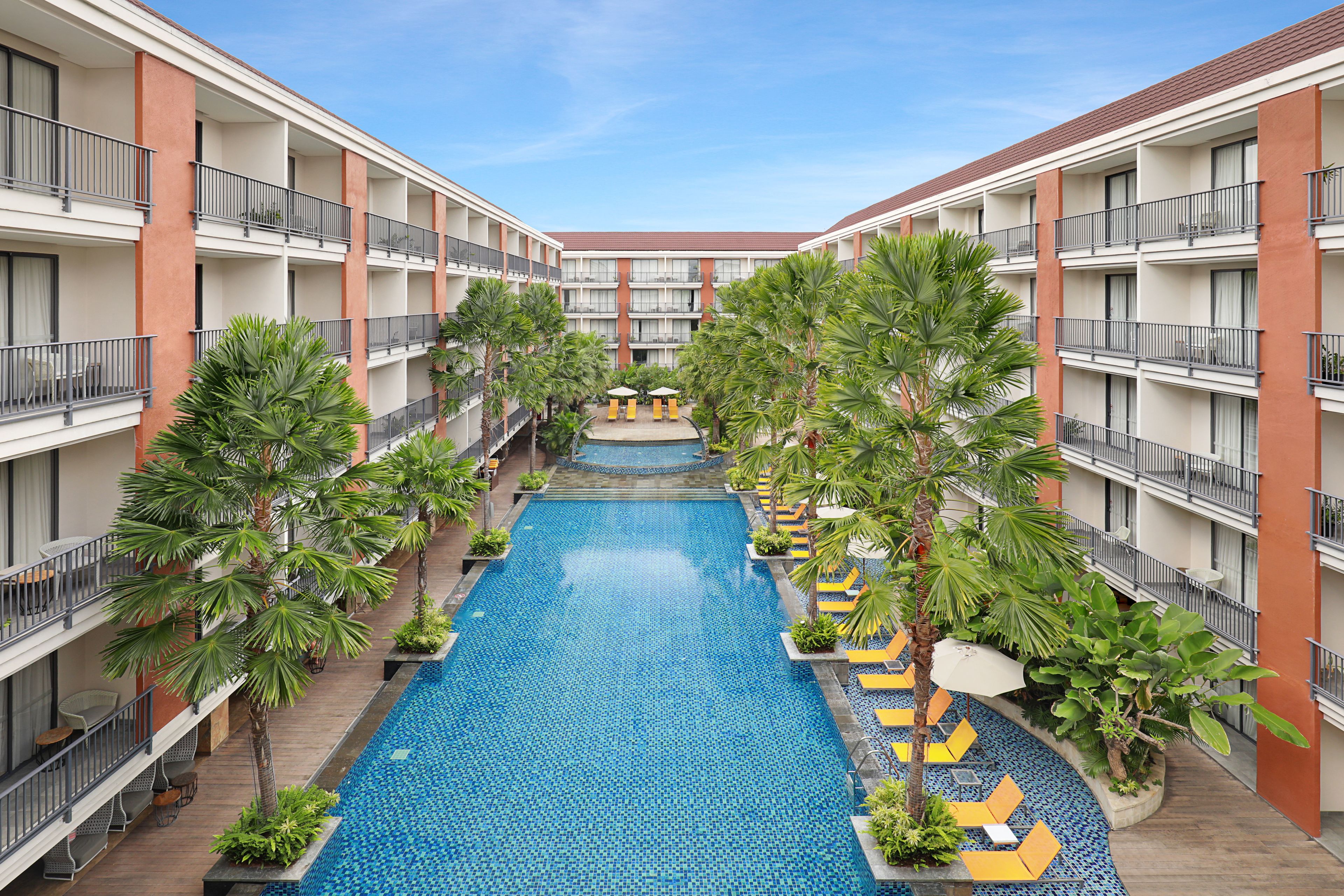 A hotel with a central swimming pool, multiple balconies, and lush greenery.