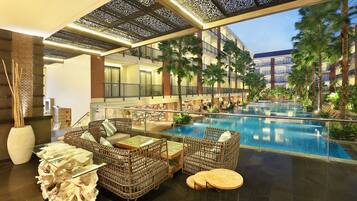 A hotel lobby with a pool, wicker furniture, and a glass coffee table.