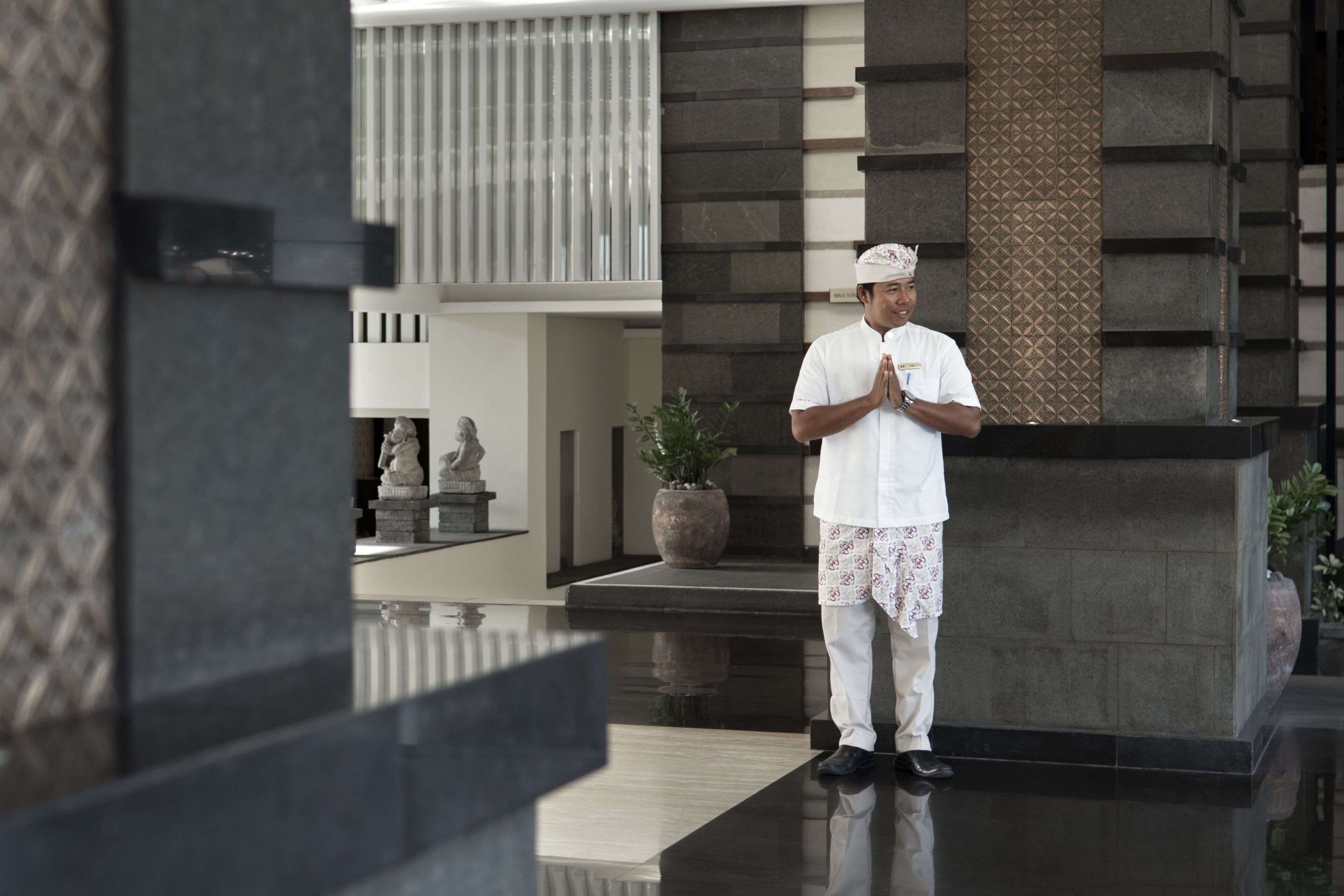 A man in traditional attire standing in a modern lobby with stone columns and a reflective floor.