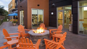 An outdoor seating area with a stone fire pit and orange Adirondack chairs. - Fairfield Inn & Suites Athens (Athens)