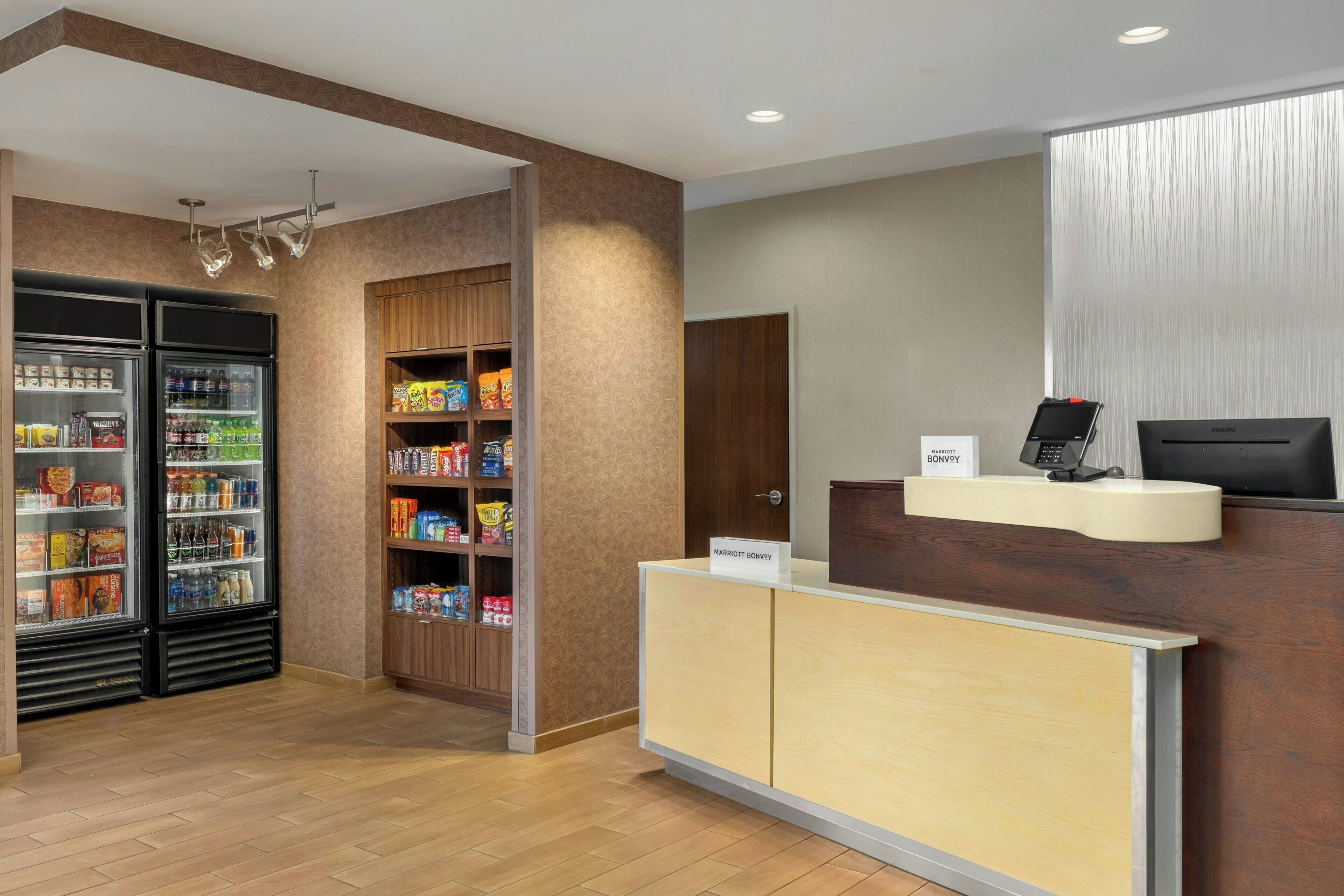 A hotel reception area with a reception desk, a minibar, and a refrigerator stocked with snacks and beverages.