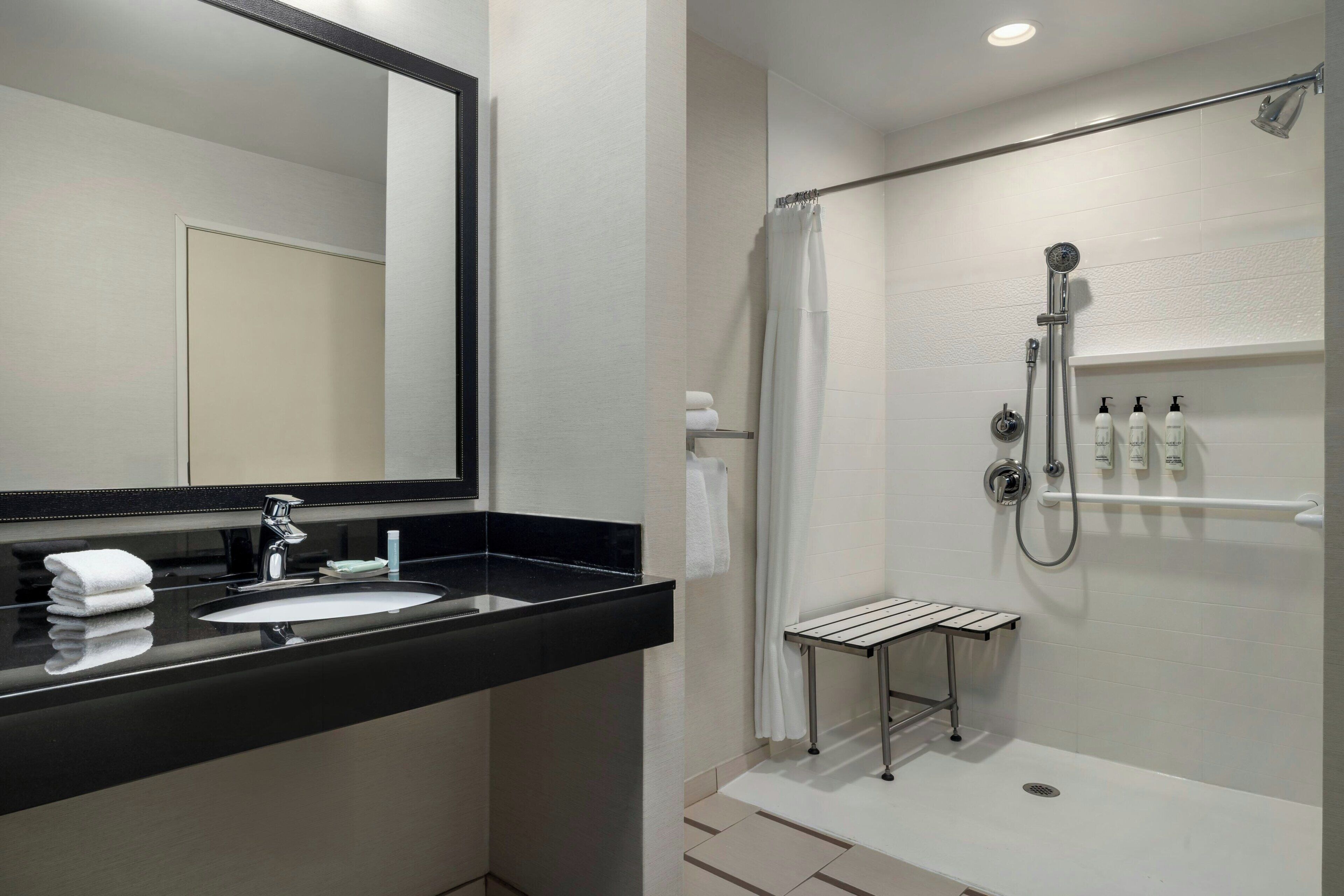 A modern bathroom with a black countertop sink, a mirror, a shower with a handheld showerhead, and a towel rack.