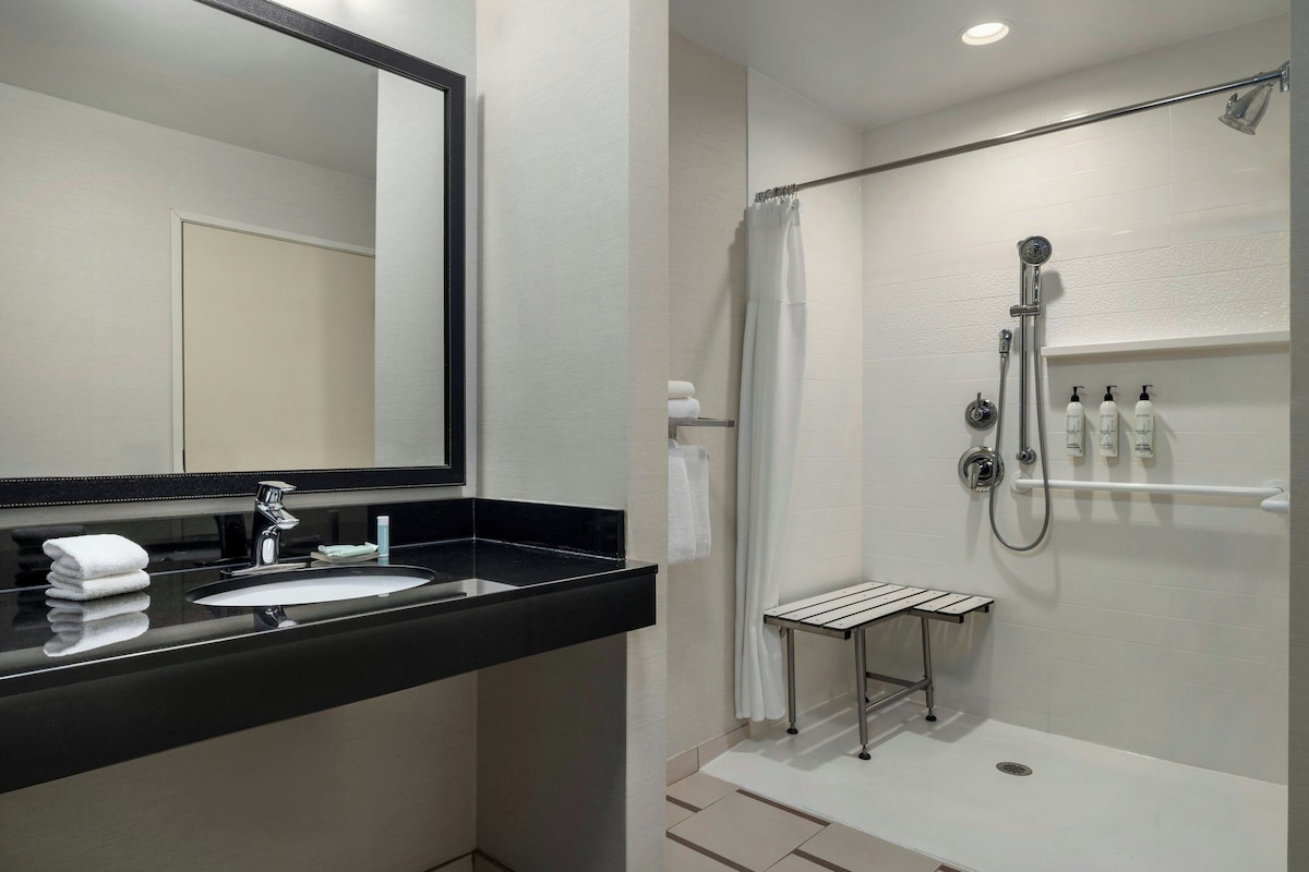 A modern bathroom with a black countertop sink, a mirror, a shower with a handheld showerhead, and a towel rack.