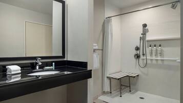 Un baño moderno con lavamanos de encimera negro, un espejo, ducha con cabezal de ducha manual y toallero.