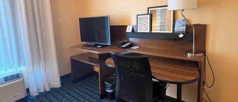Habitación de hotel con escritorio, silla, televisión y alfombra estampada.