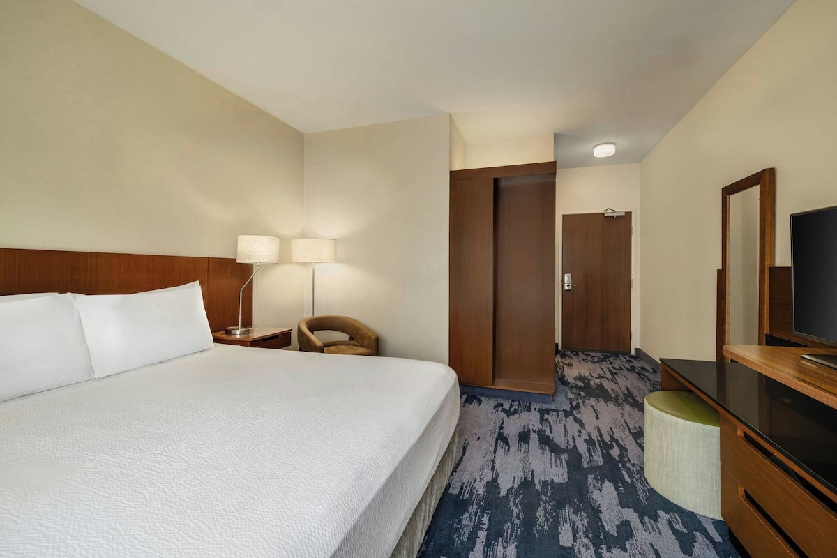 A hotel room with a large bed, a desk with a lamp, a television, and a wardrobe.