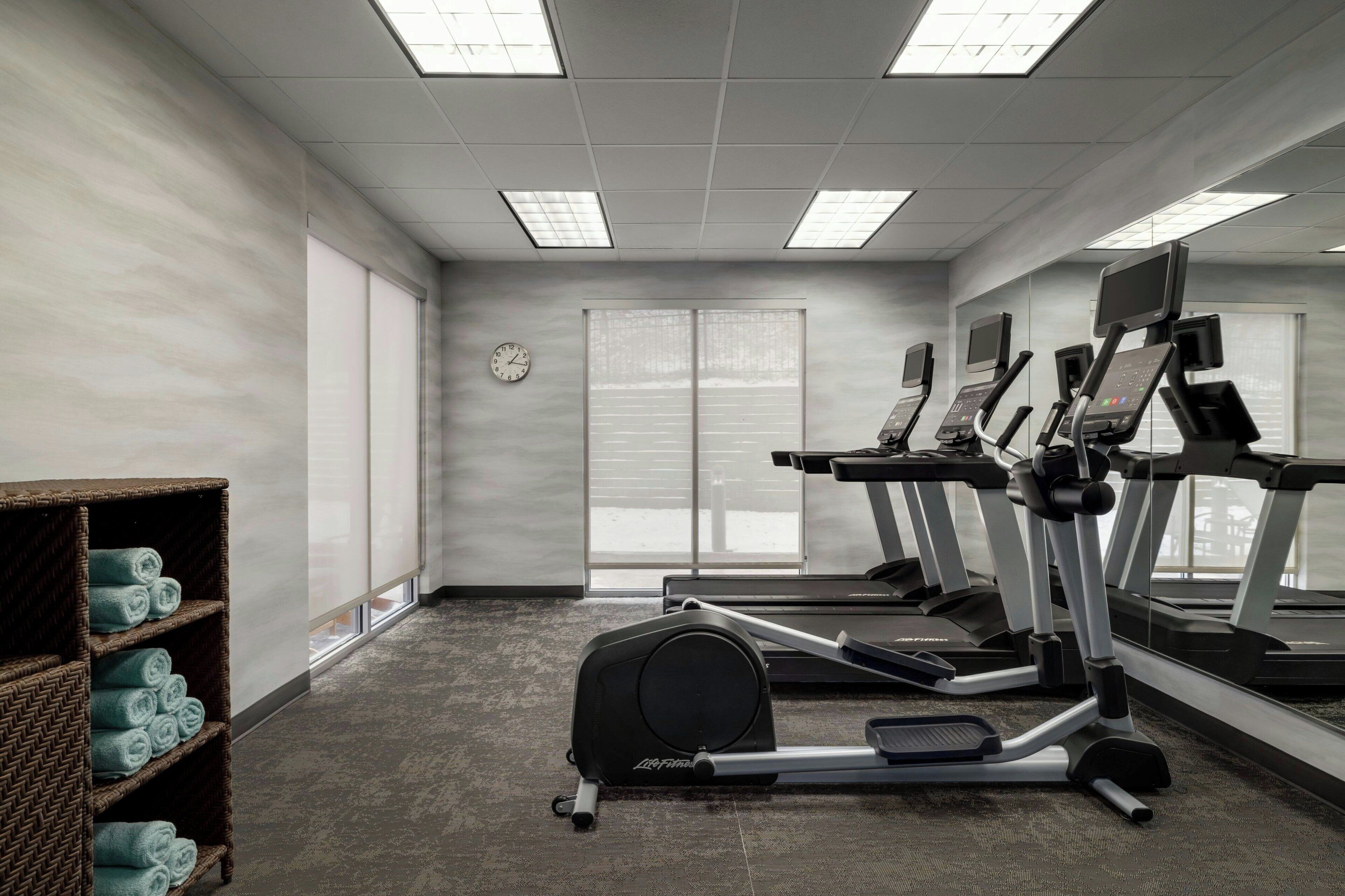 A gym with treadmills, an elliptical, and a mirrored wall.
