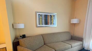 A hotel room with a beige sofa, a framed picture on the wall, two floor lamps, and a patterned carpet.