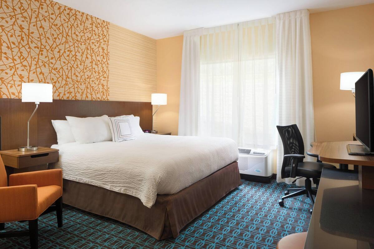 A hotel room with a large bed, two bedside lamps, a desk with a computer, a chair, and a television.