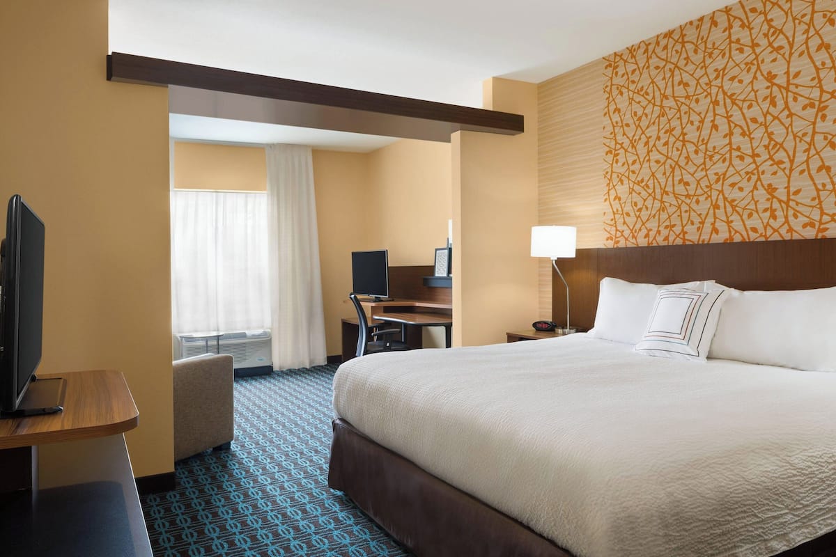 A hotel room with a large bed, a desk with a computer, a television, and a chair.