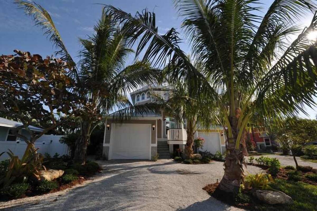 A two-story house with a covered driveway, surrounded by palm trees and a well-maintained garden.