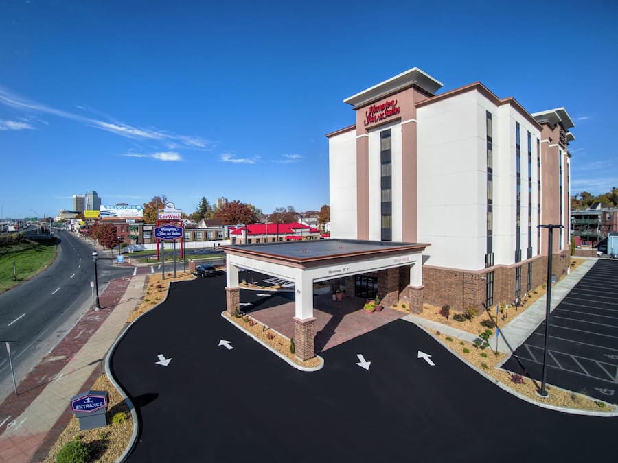 A Hampton Inn & Suites with a clear sky, a parking lot with directional arrows, and a visible entrance sign.
