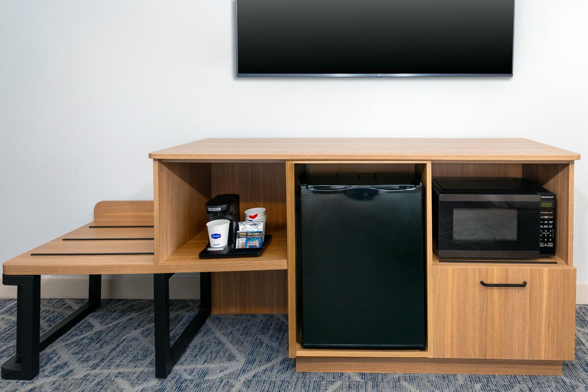 Una kitchenette compacta con microondas, cafetera y espacio para café en cápsulas.
