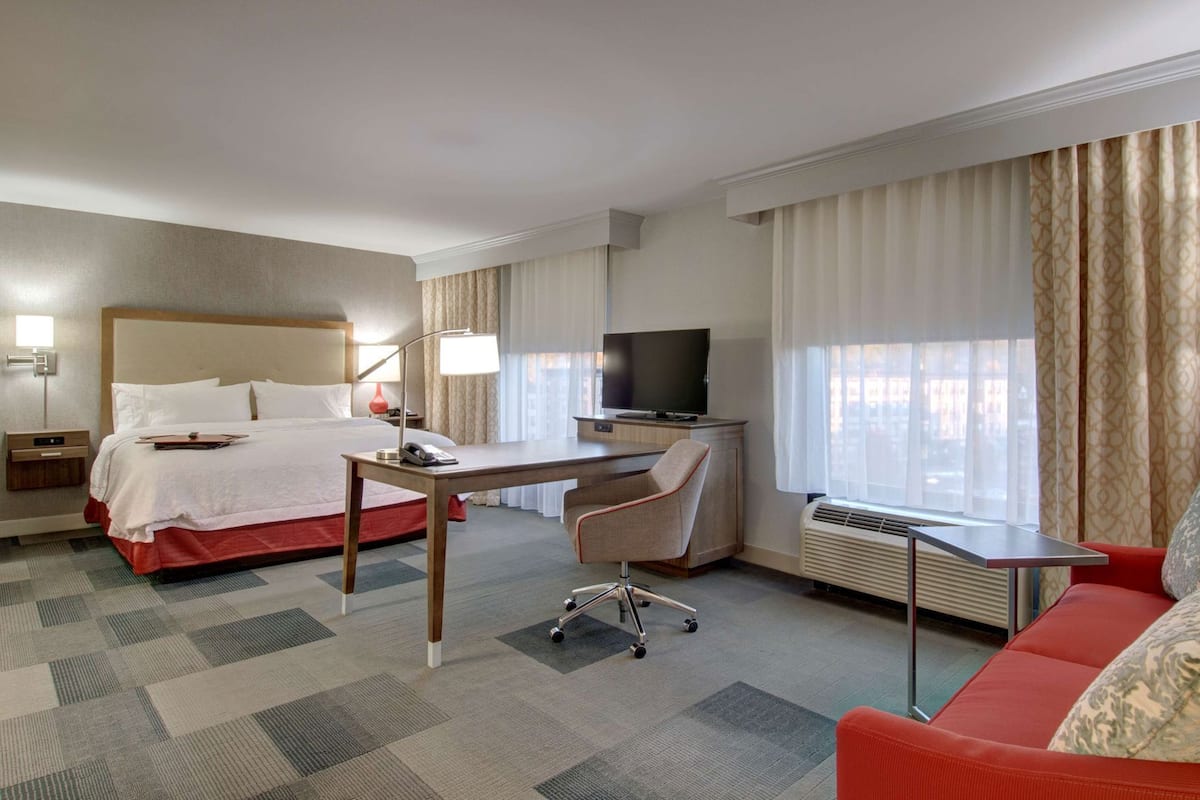 A hotel room with a bed, desk, chair, TV, and a red sofa.