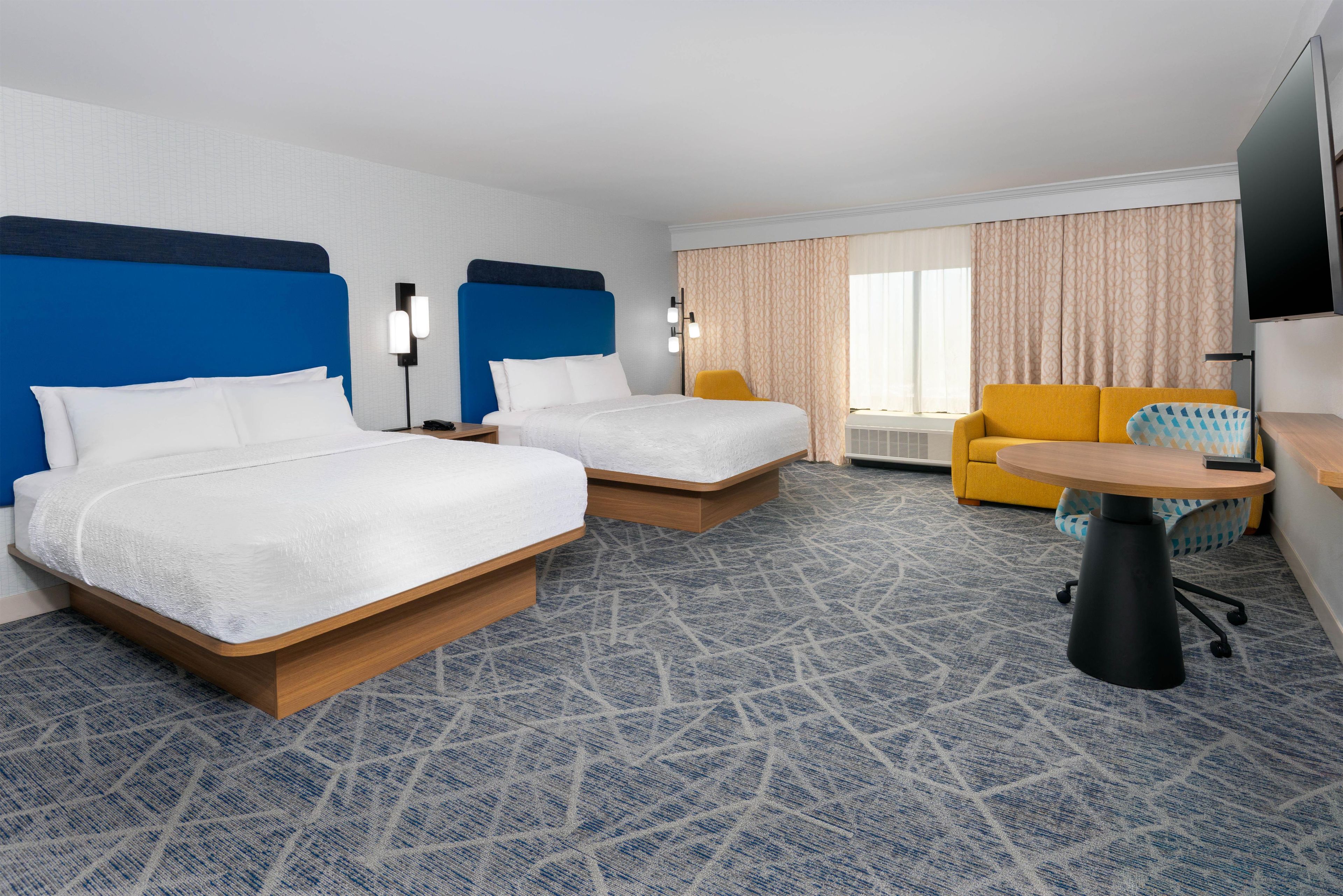 Una habitación de hotel con dos camas, un sofá, una mesita y un televisor.