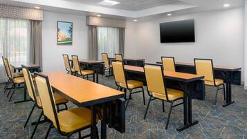 A conference room with tables and chairs, a flat-screen TV, and a painting on the wall.
